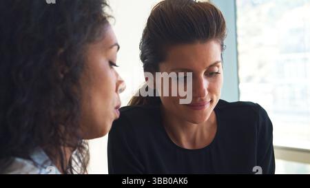 Close Up Of Two Female Business Colleagues Sitting At Desk In Office Working At Desk Together Stock Photo