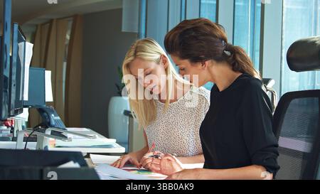 Two Female Business Colleagues Sitting At Desk In Office Discussing Documents Stock Photo