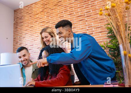 Multicultural Group of Young Friends Smiling and Interacting Laptop Indoors Stock Photo