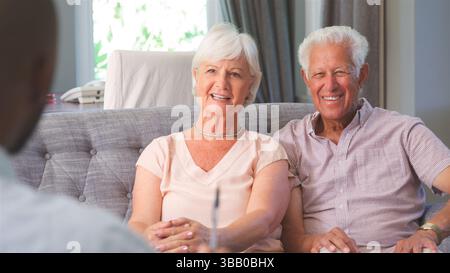 Retired Couple At Home Meeting With Financial Advisor To Discuss Investments Pension And Savings Stock Photo