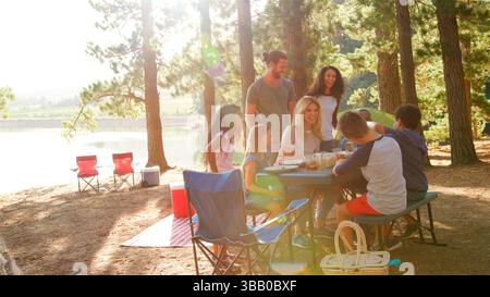 Two Familes Having Picnic Camping By Lake On Hiking Adventure In Forest Stock Photo