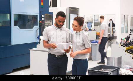 Male And Female Engineers Discussing Plans On Floor Of Engineering Workshop Stock Photo