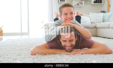Portrait Of Laughing Son Lying On Father's Back In Lounge Stock Photo