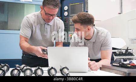Male Engineer And Apprentice Checking Components Whilst Looking At Laptop Stock Photo