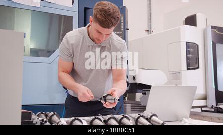 Male Engineer Measuring Components Whilst Looking At Laptop Stock Photo