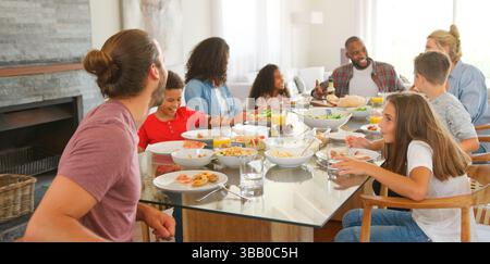 Two Families Sitting Around Table Together Enjoying Meal At Home Stock Photo