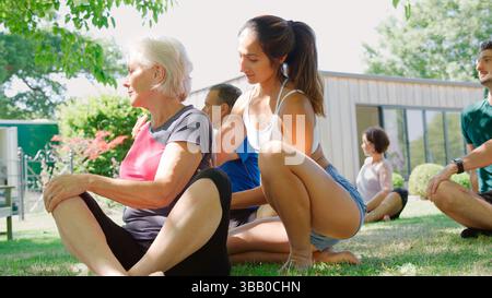 Female Instructor Helping Students At Outdoor Yoga Class Stock Photo