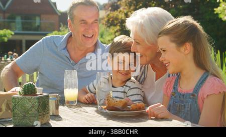 Grandparents With Grandchildren Enjoying Tea And Cake Around Table At Outdoor Café Stock Photo