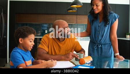 African American Parents Helping Son Studying Homework Around Table In Kitchen Stock Photo