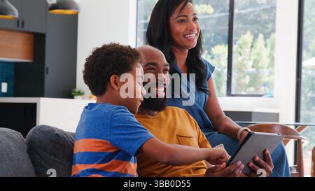 African American Family With Son Sitting On Sofa At Home Using Digital Tablet Stock Photo