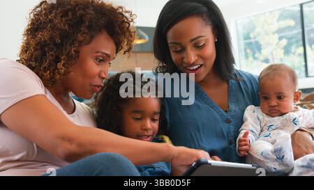 Multi-Generation Female African American Family Sitting On Sofa At Home Watching TV Together Stock Photo