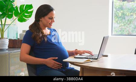 Pregnant Woman Using Laptop At Table Working From Home Stock Photo