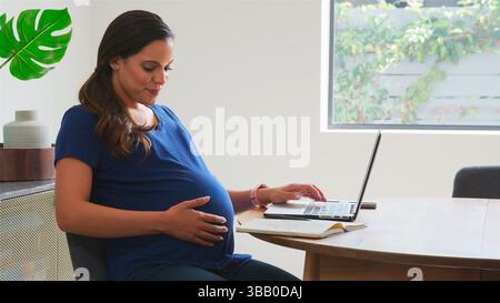 Pregnant Woman Using Laptop At Table Working From Home Stock Photo