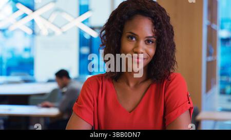 Portrait Of Smiling Businesswoman Working At Desk In Modern Open Plan Office Stock Photo