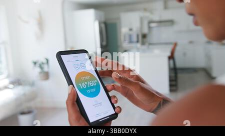 Close Up Of Woman Controlling House Central Heating Temperature Using App On Mobile Phone Stock Photo