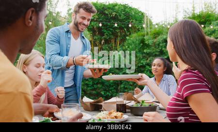 Multi-Cultural Friends At Home Sitting At Table Enjoying Food At Summer Garden Party Stock Photo