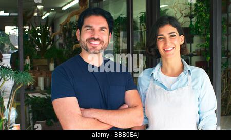 Portrait Of Male And Female Owners Of Florists Standing In Doorway Surrounded By Plants Stock Photo