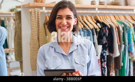 Portrait Of Female Owner Of Fashion Store Using Digital Tablet To Check Stock In Clothing Store Stock Photo