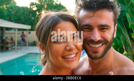 Portrait Of Romantic Hispanic Couple Outdoors With Friends Enjoying Summer Pool Party Stock Photo