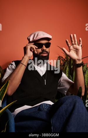 A fashionable young man wearing sunglasses and a cap enjoys a relaxed moment surrounded by greenery. Stock Photo