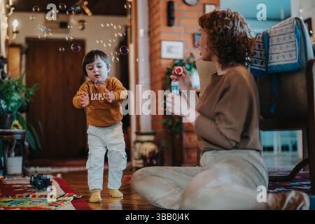 Mother and child enjoying time together blowing soap bubbles indoors in a cozy setting. Stock Photo