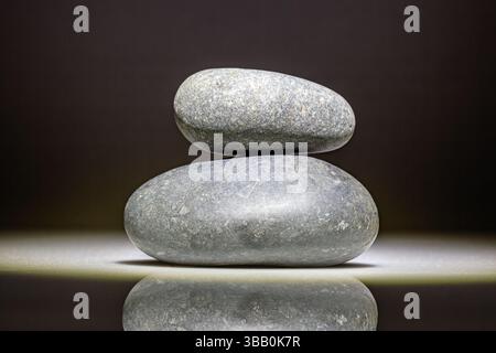 two rounded stones stacked on top of each other against a dark background Stock Photo