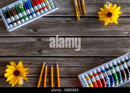 Assorted Art Supplies on Wooden Background. A flat lay of assorted art supplies on a rustic wooden background, featuring watercolor paint tubes Stock Photo