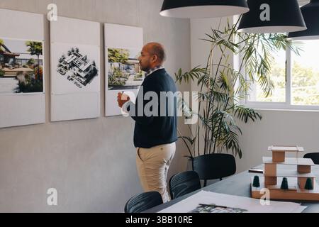 An architect examines building designs at a project planning meeting, focusing on details and strategies. Concentration and project development in an Stock Photo