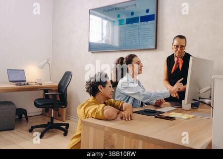 Three professional colleagues collaborate on a project while viewing a screen in an office. The setting highlights teamwork, communication, and projec Stock Photo
