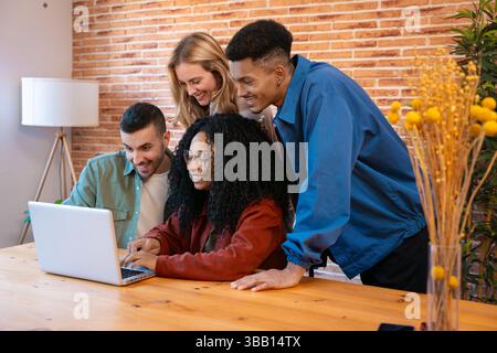 Multicultural Group of Friends Smiling While Using Laptop at Cozy Indoor Table Stock Photo