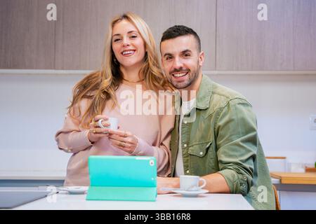 Smiling Couple Drinking Coffee and Using Tablet Together in Bright Modern Kitchen Stock Photo