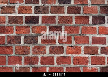 A close view of a brick wall displaying an array of red and brown bricks. The uneven texture and different shades create a rustic feel, typical in urb Stock Photo