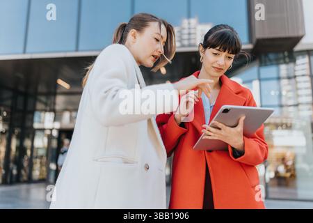 Two Businesswomen Collaborating Outdoors Using A Digital Tablet During A Discussion Stock Photo