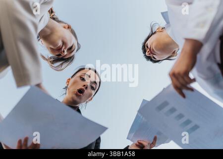 Three women collaborating outdoors, sharing and reviewing business documents together Stock Photo
