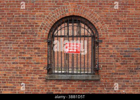Historic arched window with iron bars and a red "No Standing Anytime" sign on a red brick wall in New York City. Stock Photo