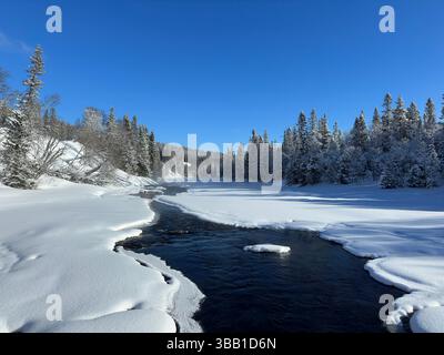Winter scene showcases a river flowing through a snowy landscape under a clear sky in north Sweden. Stock Photo