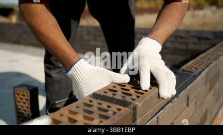 Construction worker carefully laying bricks on fresh cement, using precise hammer and level techniques while building sturdy wall section with profess Stock Photo