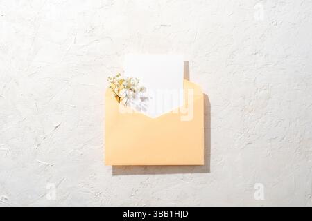 Yellow envelope with white paper and flowers on light textured background. Top view, flat lay, mockup. Stock Photo