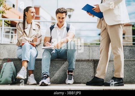 High school students collaborating outdoors with professor assisting Stock Photo