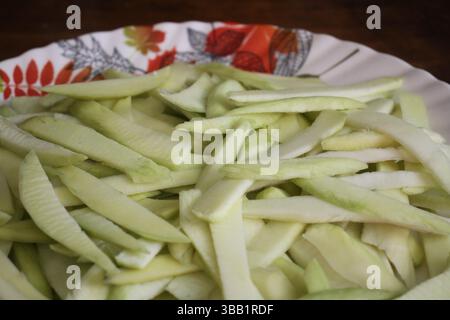 A plate is full of sliced green mangoes on the wooden surface. Stock Photo