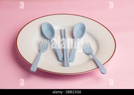Pale White Plate with Grey Spoon, Chopsticks and Fork in one plate on Pink background Stock Photo