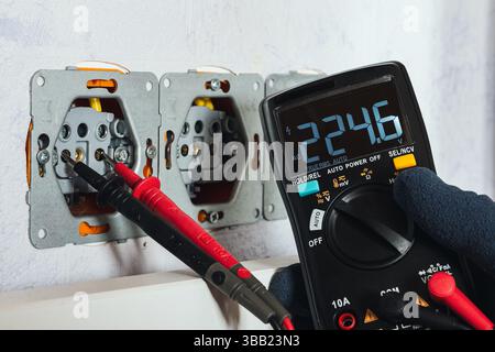 Multimeter (voltmeter) measuring voltage in a wall socket — practical demonstration of electrical testing, safety, and home diagnostics. Stock Photo