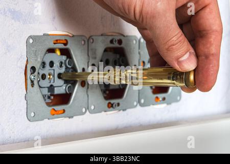 Using a voltage tester screwdriver to check for live phase in a wall socket — illustrating safety inspection and electrical diagnostics at home or on Stock Photo