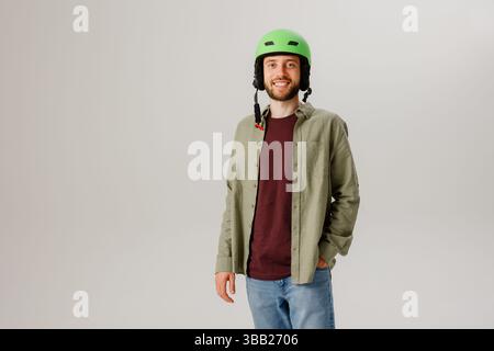 Young man dressed casually with a green helmet poses confidently in a studio setting while smiling Stock Photo