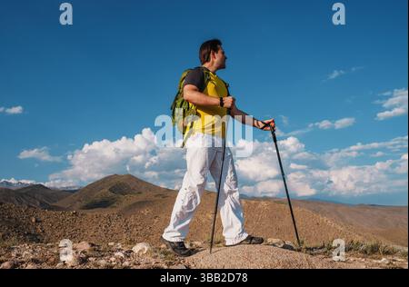 Man hiker with backpack and trekking poles standing in the mountains Stock Photo