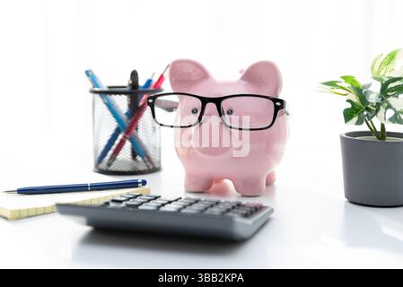 Smart piggy bank wearing glasses, using calculator, calculating finances Stock Photo