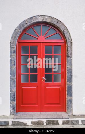 Vibrant Red Double Door with Arched Stone Frame. Eye-catching bright red double doors with glass panes set within a rustic arched frame made of grey s Stock Photo