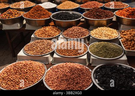 A broad variety of nuts, seeds, and dried fruits arranged in metal bowls and white pedestals at a traditional Turkish open-air market on a sunny day Stock Photo