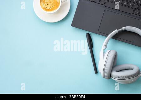 Office workspace with laptop, headphones, notepad and coffee cup. Flat lay image on blue with copy space. Stock Photo