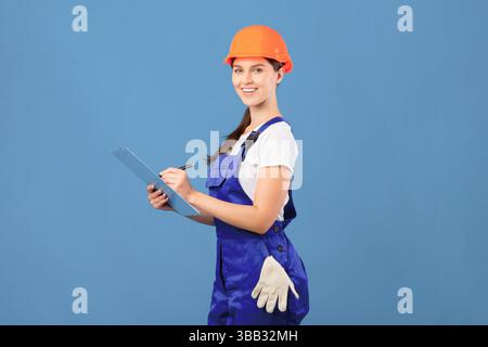 Portrait Of Happy Maintenance Worker Lady In Coverall And Hardhat With Clipboard Stock Photo